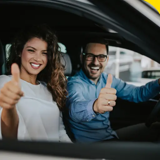 Smiling man and woman giving thumbs up in a car